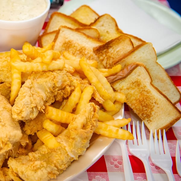 Saucy's fried chicken tenders and french fries with toast and dipping sauce on a red checkered tablecloth.