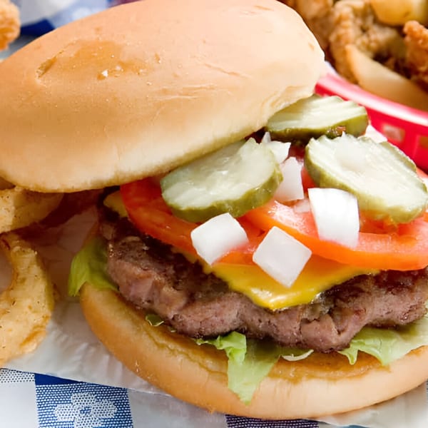 A Saucy's burger with cheese, lettuce, tomato, onions, and pickles, served with onion rings.