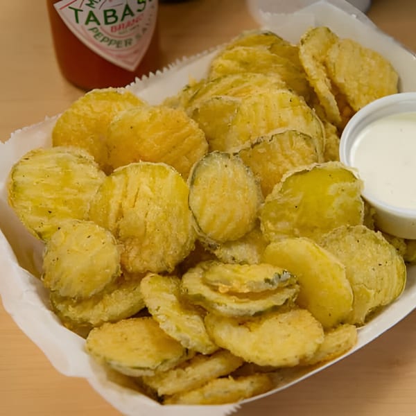 A basket of Saucy’s golden-fried pickles with a side of ranch dressing and a Tabasco bottle.